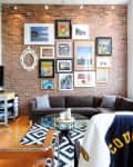 A brick wall with many pictures on it behind a couch.