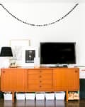 Mid-century modern console with TV, black lamp, framed art, and decorative items, flanked by shelves and doorway to bedroom.