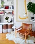 Cozy reading nook with leather chair, white rug, bookshelves, large abstract art, and a potted plant.