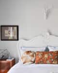 White ornate headboard with decorative pillows, framed art, and geometric decor on bedside tables.