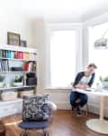 Cozy living room with a round table, two people chatting, bookshelves, a bull skull, and a vase of orange flowers.