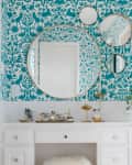 One large round mirror surrounded by three smaller round mirrors on a wall with teal patterned wallpaper