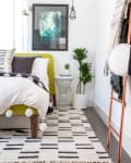 Modern bedroom with a yellow bed, black and white decor, abstract art, and a potted plant on a geometric side table.