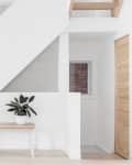 Wooden bench with potted plant under a modern staircase in a minimalist room.