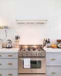 Modern kitchen with stainless steel stove, open shelves, toaster, kettle, and espresso machine on white countertops.