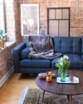 Cozy living room with a blue sofa, fur throw, brick walls, and a wooden coffee table with flowers and decor items.