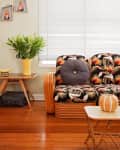 Rattan sofa with floral cushions, round pillow, side table with plant, and framed art on wall.