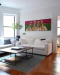 Modern living room with white sofas, abstract art, wooden table, pendant lights, and a potted plant by the window.
