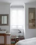 Bedroom with a wooden desk, books, framed mirror, and abstract wall art near a window with white blinds.