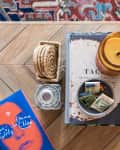 Coffee table with a candle, coasters, a book titled "The Girls," and a bowl of matchbooks on a patterned rug.