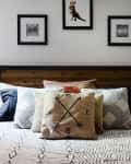 Bed with geometric patterned bedding, decorative pillows, wooden headboard, and framed art on the wall.
