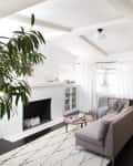 Bright living room with gray sectional sofa, white fireplace, black door, and large plant.