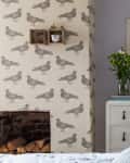 Bedroom with pigeon wallpaper, white dresser, orange lamp, vase of flowers, and framed bird print.