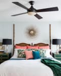 Bedroom with a sunburst mirror, green nightstands, black lamps, and a bed with floral and coral pillows.