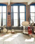 Loft studio with brick walls, large windows, ceramic plates on wall, and pottery equipment.
