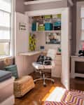 Home office nook with white desk, swivel chair, storage boxes, and decor in a closet space with open doors.