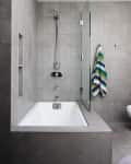 Modern bathroom with a tiled bathtub, glass shower screen, and colorful zigzag towel hanging on the wall.