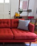Red mid-century modern sofa with two gray patterned pillows in a living room with lockers and a console table.