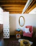Cozy living area with a pink armchair, gold oval mirror, wooden side table, and a blue record player.