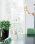 Dining room with green chairs, black table, gold chandelier, large window, and abstract wall art.