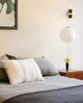 Bedroom with gray bedding, striped pillow, wall art, globe lamp, and wooden nightstand with a yellow flower in a vase.