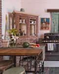 Rustic kitchen with vintage fridge, wooden cabinets, green distressed door, and a table with flowers, watermelon, and apples.