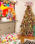 Festive living room with a decorated Christmas tree, colorful art, green sofa, and holiday-themed decor.