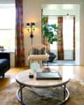 Living room with marble coffee table, fur rug, patterned curtains, wall sconce, and a potted plant by the window.