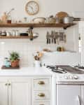 Rustic kitchen with white cabinets, brick accent, open shelves, vintage stove, and various kitchenware.