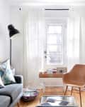Bright living room with a gray sofa, patterned pillows, tan chair, and white curtains.