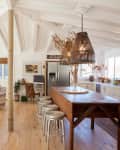 Open-concept living room and kitchen with wooden island, wicker pendant lights, beige sofas, and rustic decor.