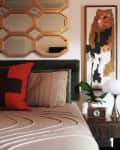 Bed with beige textured blanket, orange and brown pillows, gold hexagonal mirror, abstract art, and orchid on nightstand.