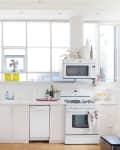 Bright kitchen with white cabinets, a gas stove, microwave, and hanging decorative bells.