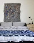 Bedroom with a double bed, gray bedding, blue patterned throw, abstract wall art, and wooden nightstands with lamps.