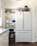 White kitchen with a double-door fridge, open shelves with dishes, and a countertop mixer.