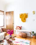 Living room with brown leather sofa, colorful pillows, wooden coffee table, round mirror, and yellow macrame wall hanging.
