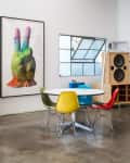 Modern dining area with colorful chairs, round table, large artwork, and speaker system.