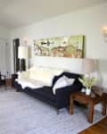 Black sofa with white fur throw, wooden side table, lamps, and abstract wall art in a living room.