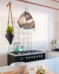 A copper pipe above a kitchen island with S-hooks holding kitchen utensils, a strainer, and a plant