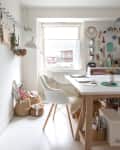 Home office with a white chair, wooden desk, pegboard with tools, and baskets by the window.