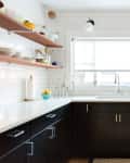 Modern kitchen with black cabinets, white countertops, open wooden shelves, and stainless steel dishwasher.