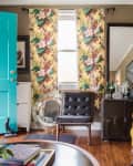Living room with turquoise door, yellow sofa, floral curtains, black chair, and a vintage trunk bar setup.