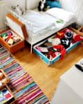 Children's bedroom with a single bed, colorful rug, and organized toy storage boxes under the bed.