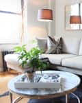Modern living room with a beige sofa, geometric pillows, floor lamp, marble coffee table, and potted plant.