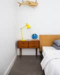 Mid-century modern bedroom with wooden nightstand, yellow lamp, blue clock, and hanging wooden whale decor.