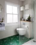 A bathroom with a glass shower door and green floor tiles with a geometric pattern.