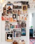 Wall-mounted bookshelf filled with colorful books and decor items, adjacent to a doorway leading to a room with a patterned rug.