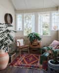 Sunroom with wicker chairs, vibrant patterned rug, potted plants, and open French doors.