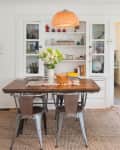 Dining room with a wooden table, metal chairs, woven pendant light, and a cabinet with decor items and books.