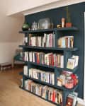 Dark blue bookshelf filled with books, glass jars, and decor items, set against a wooden floor and white wall.